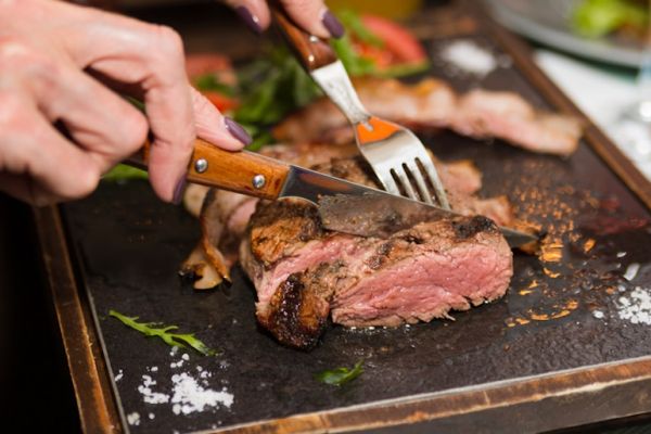 Mature woman cutting grass-fed meat for dinner, one of the best foods on the Galveston Diet, to support weight loss and reduce symptoms of menopause