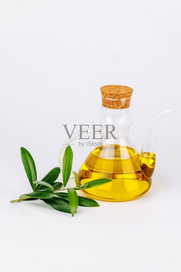 健康的橄欖油裝在玻璃瓶中，旁邊有新鮮的橄欖枝，背景為白色。照片攝影圖片