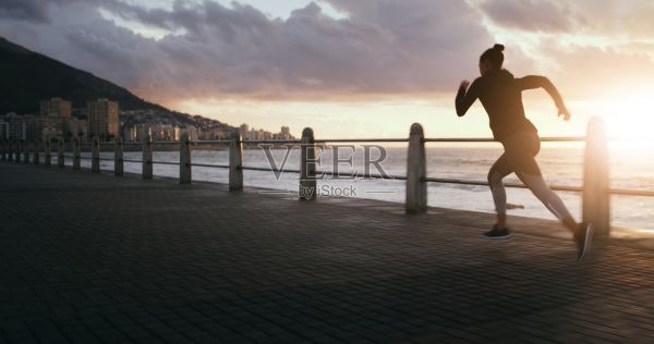 女性在海滩日落时跑步健身，沿着海滨长廊进行有氧运动和户外减肥。女性运动员在大自然中训练，进行空间挑战和练习例行。照片摄影图片