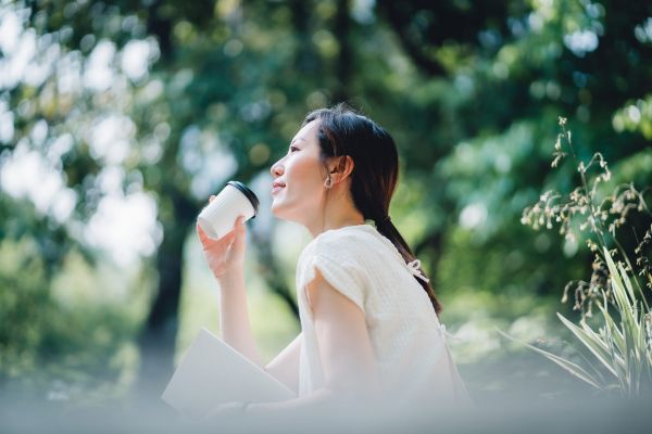 young asian woman sitting on a bench in park, reading a book and having a relaxing time enjoying the sunny day outdoors in the city. enjoying a technology free moment
