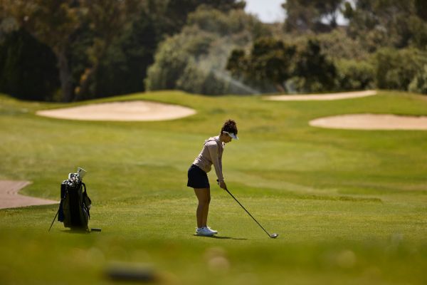 side view of female golfer taking shot for putting golf ball in green at course