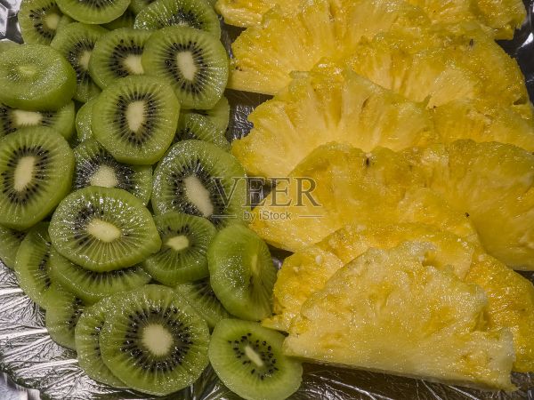 專(zhuān)業(yè)廚房里，玻璃盤(pán)上擺放著新鮮的菠蘿和獼猴桃切片，這是一份充滿(mǎn)活力的熱帶水果拼盤(pán)，可作為餐廳服務(wù)的健康零食或甜點(diǎn)。照片攝影圖片