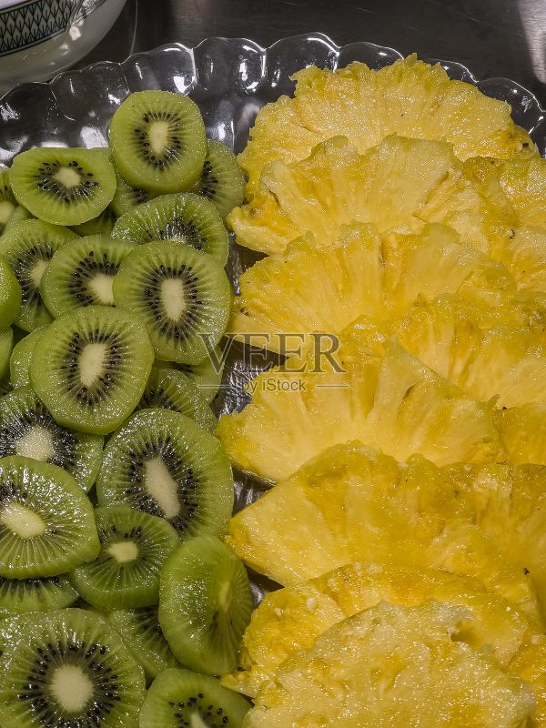 专业厨房里的玻璃盘上摆放着新鲜的菠萝和猕猴桃切片，这是为餐厅服务准备的充满活力的热带水果拼盘，可作为健康的零食或甜点。照片摄影图片