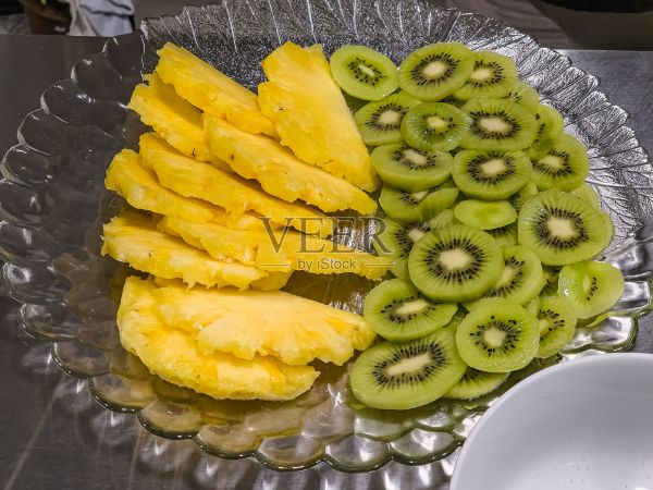 專(zhuān)業(yè)廚房的玻璃盤(pán)上擺放著新鮮的菠蘿和獼猴桃切片，這是為餐廳服務(wù)準(zhǔn)備的充滿(mǎn)活力的熱帶水果拼盤(pán)，可作為健康零食或甜點(diǎn)。照片攝影圖片