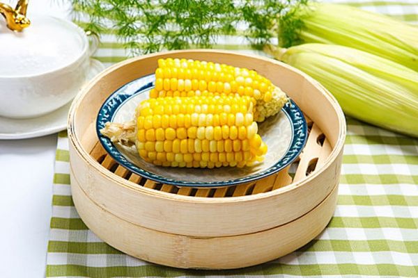 家庭厨房蒸制水果玉米：不锈钢蒸锅内玉米整齐平铺，蒸汽均匀升腾，计时器显示12:00，旁边放置刚出锅的玉米与不锈钢刀具，展现最佳食用状态