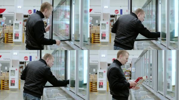 一名穿著休閑服的男子在超市冷凍柜中挑選冷凍餐。他打開和關(guān)閉冰柜的門，檢查里面的各種產(chǎn)品。一名男子在超