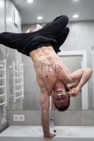 一名男子在浴室里倒立着清洁牙齿，用一只手保持平衡。健康的生活方式，健康的身体和瑜伽的理念图片