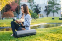 漂亮的白人女子坐在绿色的草地上，智能手机靠近健身垫。健康的生活方式概念和在新鲜空气中锻炼。健康的女人。健康的生活方式，运动。美丽的肖像。图片